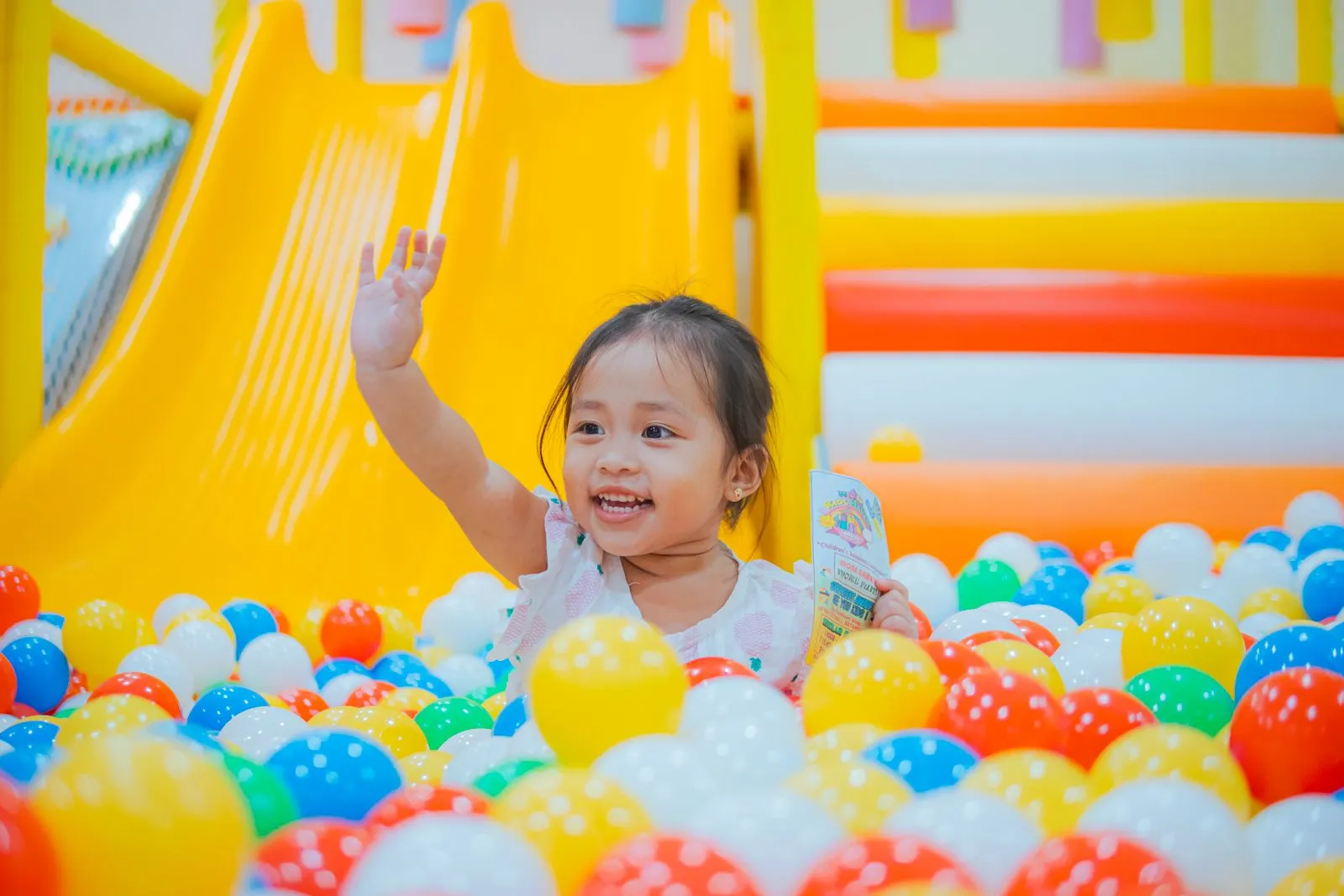 Happy child playing in a vibrant ball pit, surrounded by colorful balls and a slide, expressing fun and joy.